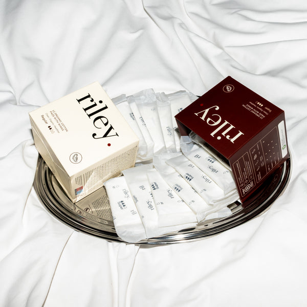 Two Riley product boxes and several pads on a round metal tray over white fabric.
